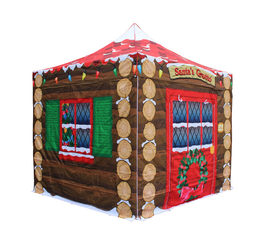 A Christmas-themed pop up gazebo shaped like a log cabin grotto, featuring a red roof with snow trim, brown wood-textured walls, log posts, green shutters, and a red door with a wreath